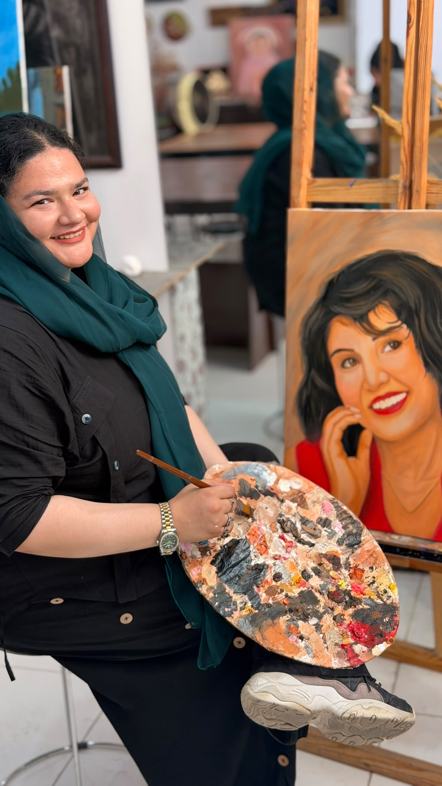 Zuhra smiling beside her finished portrait while holding her painter's palette
